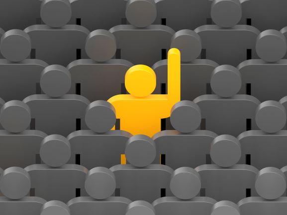 One person in large group raising a hand.  Customers and prospective customers want to help you. Just ask.