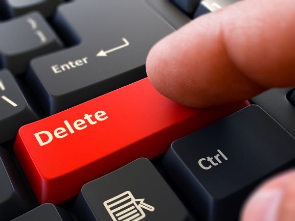 a finger pushing the delete button on a computer to streamline wordy sentences
